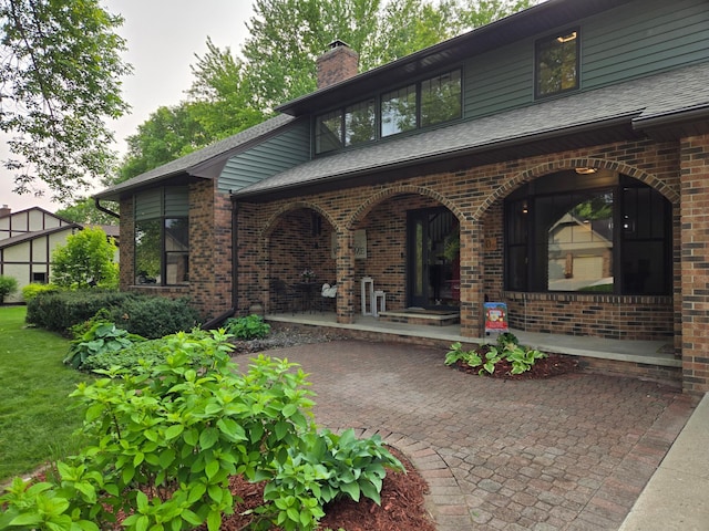 1410 16th St SW, Willmar, MN 56201 - view of exterior entry with covered porch, a chimney, brick siding, and a shingled roof