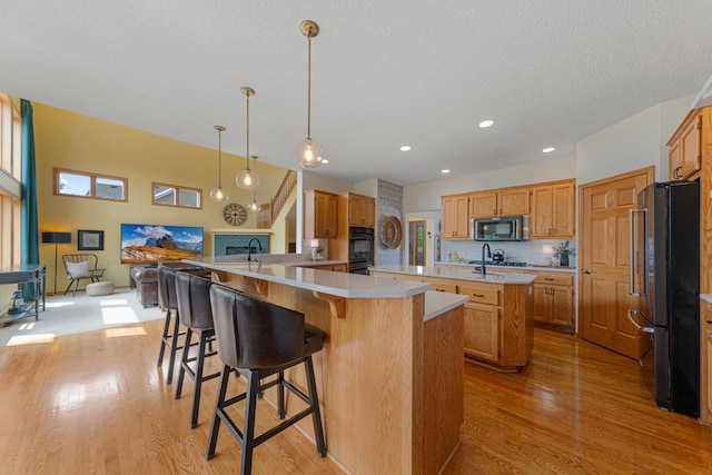 1900 Legacy Dr, Faribault, MN 55021 - kitchen with appliances with stainless steel finishes, an island with sink, light wood-style flooring, light countertops, and a kitchen bar