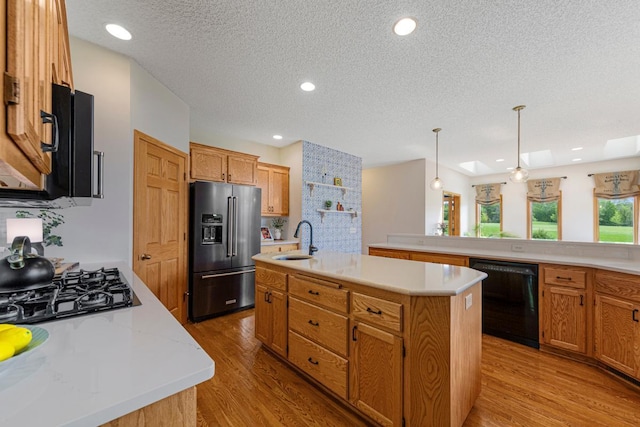 1900 Legacy Dr, Faribault, MN 55021 - kitchen featuring black appliances, a sink, an island with sink, light wood-style floors, and light countertops