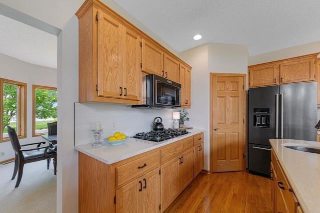 1900 Legacy Dr, Faribault, MN 55021 - kitchen featuring black appliances, light countertops, tasteful backsplash, a textured ceiling, and light wood finished floors