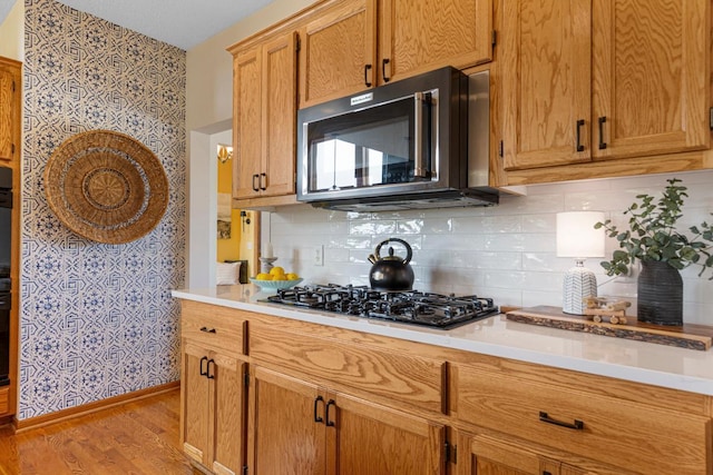 1900 Legacy Dr, Faribault, MN 55021 - kitchen featuring black appliances, wallpapered walls, light wood-type flooring, light countertops, and backsplash