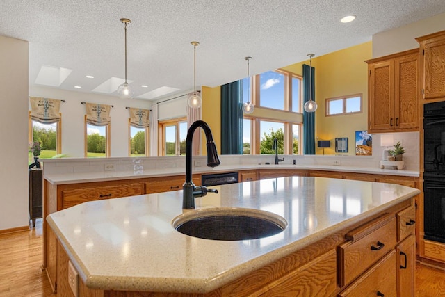 1900 Legacy Dr, Faribault, MN 55021 - kitchen with a textured ceiling, a sink, a center island with sink, brown cabinetry, and light wood-type flooring