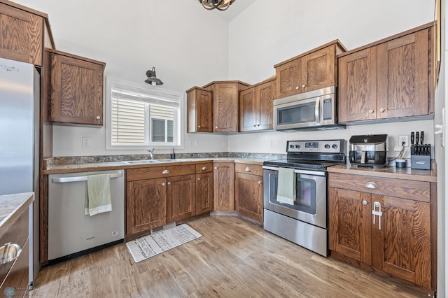 934 31st Ave W, West Fargo, ND 58078 - kitchen with appliances with stainless steel finishes, a sink, light wood-style floors, a high ceiling, and brown cabinets