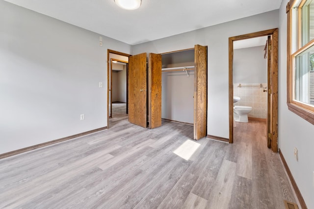 51470 Rush Lake Trl, Nessel Twp, MN 55069 - unfurnished bedroom featuring wood finished floors, a closet, tile walls, a wainscoted wall, and connected bathroom