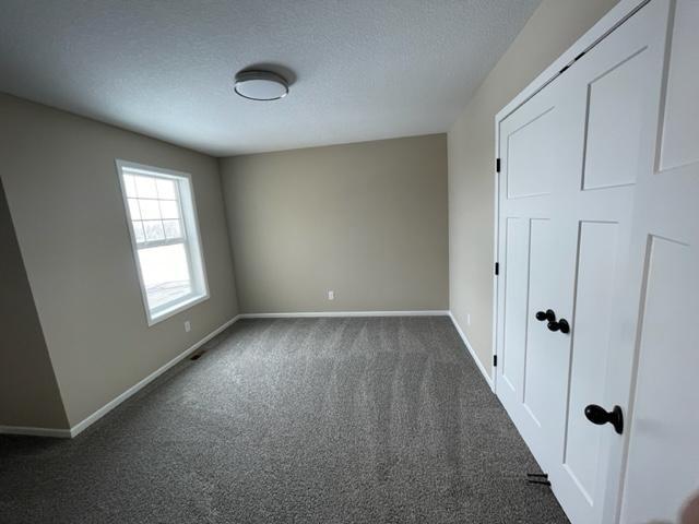 1027 45th Ave NE, Saint Cloud, MN 56304 - unfurnished bedroom with dark carpet, baseboards, a textured ceiling, and a closet