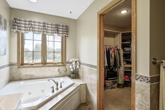 22774 Olivine St NW, Nowthen, MN 55330 - bathroom featuring a tub with jets, wainscoting, tile walls, and a spacious closet