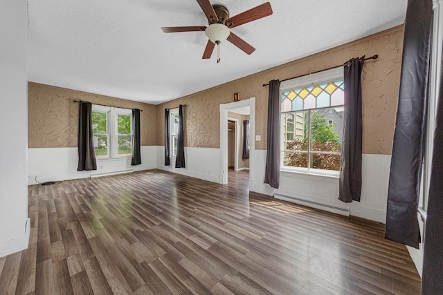 300 Ellington St, West Concord, MN 55985 - unfurnished living room featuring a baseboard radiator, a wainscoted wall, a ceiling fan, wood finished floors, and a textured ceiling