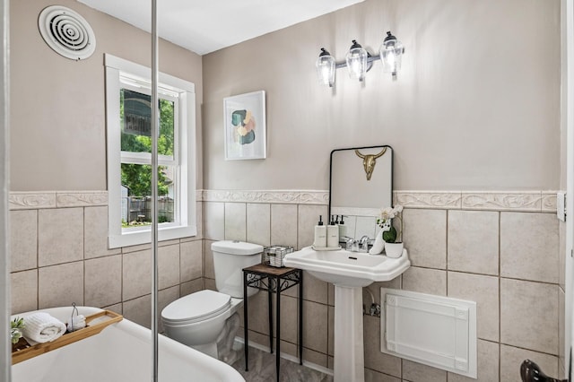 404 8th Ave S, Princeton, MN 55371 - bathroom featuring tile walls, a bath, toilet, and a wainscoted wall