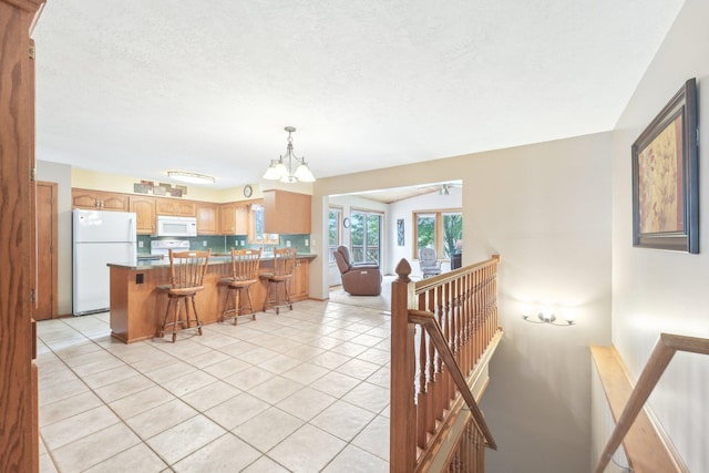 1852 13th Ave W, Shakopee, MN 55379 - kitchen with white appliances, a chandelier, a peninsula, light tile patterned floors, and a breakfast bar