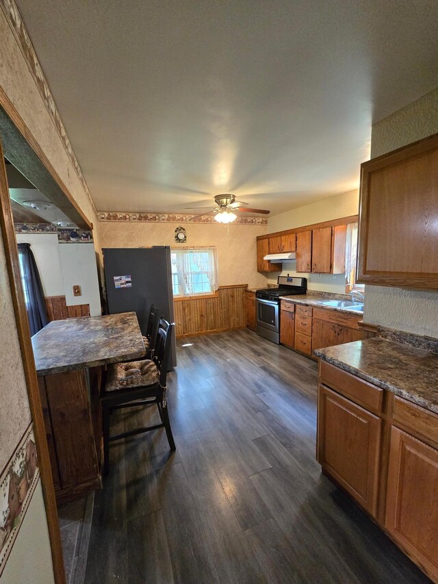 25 Morgan St, Tracy, MN 56175 - kitchen with stainless steel gas range, brown cabinets, dark wood finished floors, a ceiling fan, and under cabinet range hood
