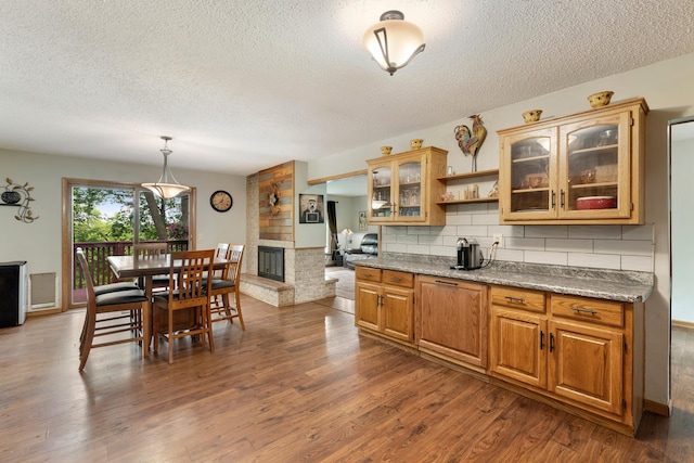 13100 Island View Dr NW, Elk River, MN 55330 - kitchen with a textured ceiling, dark wood finished floors, glass insert cabinets, decorative backsplash, and a multi sided fireplace
