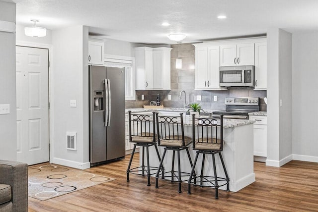 320 Ford Rd Unit 3, Saint Louis Park, MN 55426 - kitchen featuring appliances with stainless steel finishes, white cabinets, a breakfast bar area, wood finished floors, and a kitchen island