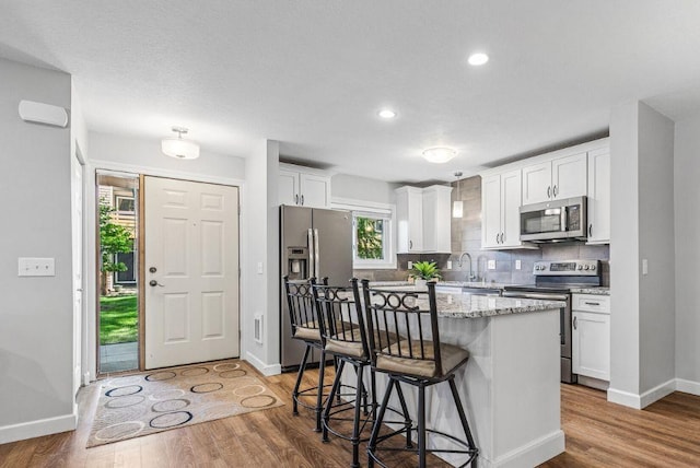 320 Ford Rd Unit 3, Saint Louis Park, MN 55426 - kitchen featuring stainless steel appliances, a kitchen breakfast bar, white cabinetry, tasteful backsplash, and wood finished floors
