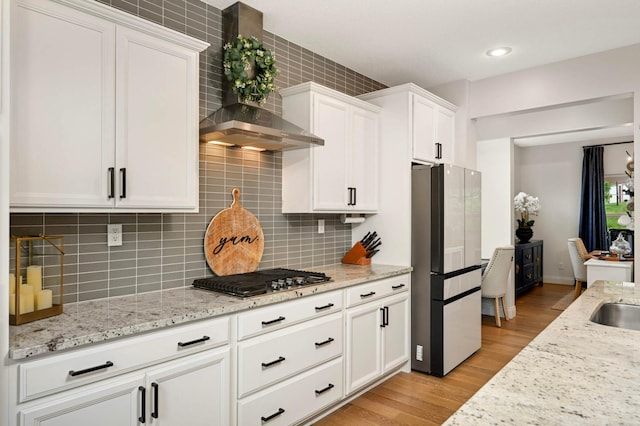 6100 151st St, Savage, MN 55378 - kitchen featuring freestanding refrigerator, wall chimney range hood, stainless steel gas cooktop, white cabinetry, and light wood-style floors