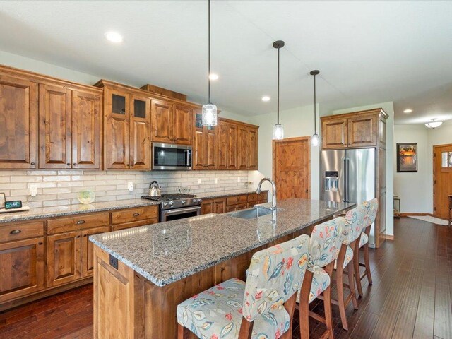 7496 Fairway Ln, Breezy Point, MN 56472 - kitchen featuring appliances with stainless steel finishes, brown cabinets, dark wood-style flooring, a breakfast bar area, and decorative backsplash