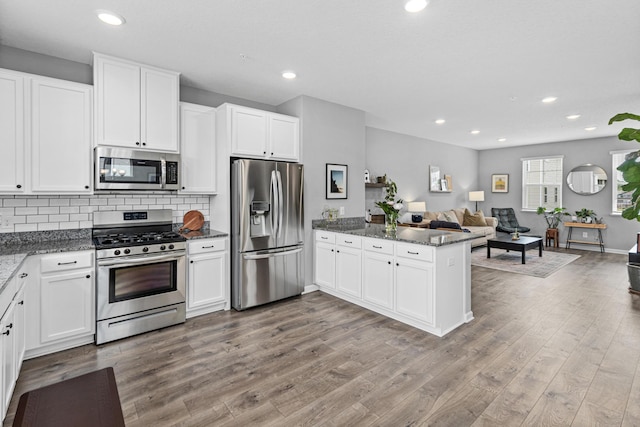 8756 Granite Ln, Woodbury, MN 55129 - kitchen featuring appliances with stainless steel finishes, a peninsula, open floor plan, white cabinetry, and tasteful backsplash