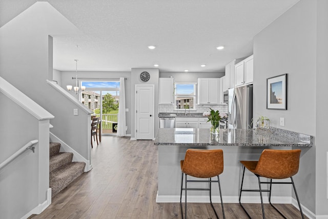 8756 Granite Ln, Woodbury, MN 55129 - kitchen with appliances with stainless steel finishes, a chandelier, dark stone countertops, white cabinets, and a peninsula