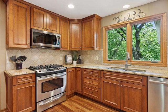 5921 Creek Pt, Minnetonka, MN 55345 - kitchen featuring appliances with stainless steel finishes, a sink, brown cabinets, light stone counters, and light wood-style flooring