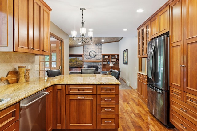 5921 Creek Pt, Minnetonka, MN 55345 - kitchen featuring stainless steel appliances, a peninsula, brown cabinets, light wood-style flooring, and a brick fireplace