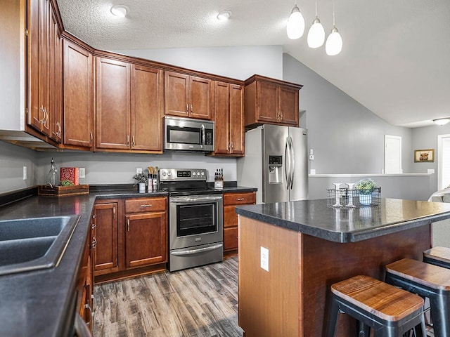 1308 Timber Ln, Buffalo, MN 55313 - kitchen featuring appliances with stainless steel finishes, vaulted ceiling, wood finished floors, dark countertops, and a breakfast bar