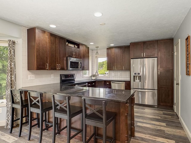 15564 Vale St NW, Andover, MN 55304 - kitchen featuring appliances with stainless steel finishes, a peninsula, a sink, dark wood-style flooring, and backsplash