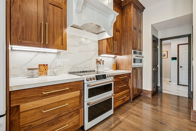 11883 Flanders Cir NE, Blaine, MN 55449 - kitchen featuring range with two ovens, premium range hood, tasteful backsplash, wood finished floors, and brown cabinetry
