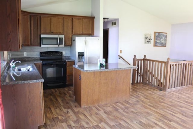 1027 Taft St S, Cambridge, MN 55008 - kitchen featuring appliances with stainless steel finishes, vaulted ceiling, wood finished floors, a kitchen island, and decorative backsplash