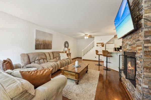 9955 Russell Ave N Unit 10, Brooklyn Park, MN 55444 - living room featuring stairs, dark wood-style flooring, ceiling fan, baseboards, and a stone fireplace