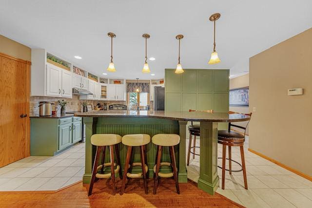 1525 21st Ave NW, Faribault, MN 55021 - kitchen featuring freestanding refrigerator, decorative backsplash, a breakfast bar, white cabinetry, and under cabinet range hood