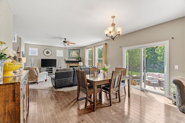 14143 Ailesbury Ave, Rosemount, MN 55068 - dining area featuring a stone fireplace, wood finished floors, a ceiling fan, and a chandelier
