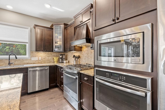 14143 Ailesbury Ave, Rosemount, MN 55068 - kitchen featuring stainless steel appliances, custom exhaust hood, light wood-style flooring, dark brown cabinetry, and recessed lighting