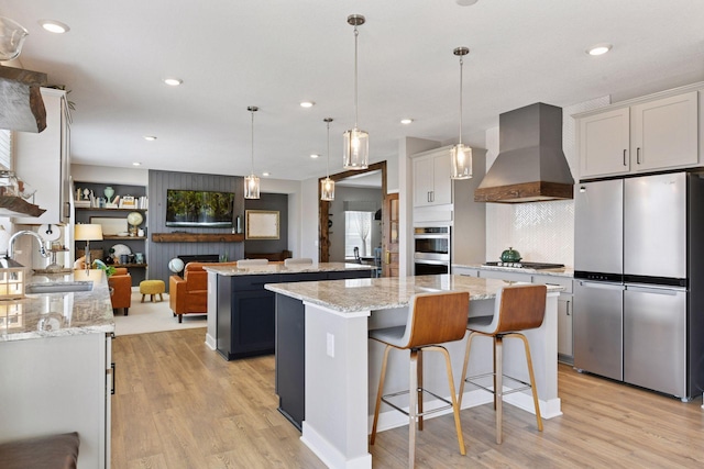 515 Goldenrod Trl, Waconia, MN 55387 - kitchen featuring stainless steel appliances, wall chimney exhaust hood, a sink, a kitchen island, and light wood-style floors