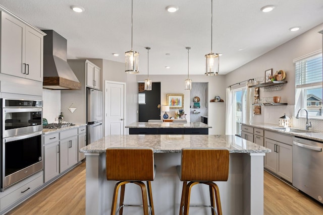 515 Goldenrod Trl, Waconia, MN 55387 - kitchen with a sink, a kitchen island, wall chimney exhaust hood, appliances with stainless steel finishes, and light wood-type flooring