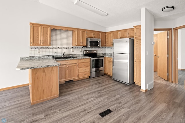 2831 Wheatland Dr S, Fargo, ND 58103 - kitchen with appliances with stainless steel finishes, a sink, a peninsula, light wood-style floors, and backsplash