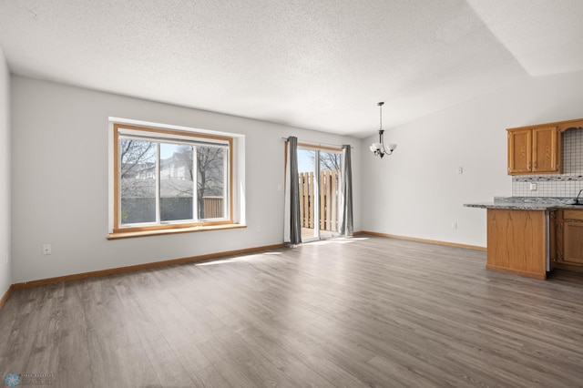 2831 Wheatland Dr S, Fargo, ND 58103 - unfurnished living room with a chandelier, plenty of natural light, wood finished floors, a textured ceiling, and vaulted ceiling