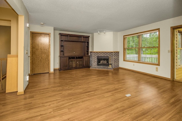 4906 Bayswater Rd, Minnetonka, MN 55345 - unfurnished living room featuring light wood-type flooring, a textured ceiling, a brick fireplace, baseboards, and rail lighting