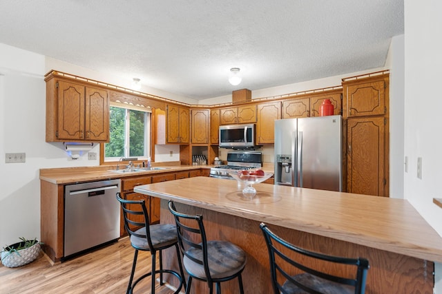 20195 Harrow Ave Way N, Forest Lake, MN 55025 - kitchen with stainless steel appliances, light wood-style flooring, brown cabinetry, a kitchen bar, and a peninsula