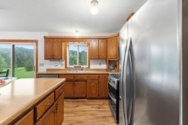 20195 Harrow Ave Way N, Forest Lake, MN 55025 - kitchen featuring stainless steel appliances, brown cabinetry, light wood-style floors, healthy amount of natural light, and a textured ceiling
