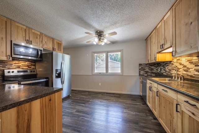 1605 4th St SW, Austin, MN 55912 - kitchen featuring appliances with stainless steel finishes, a sink, dark countertops, a ceiling fan, and wainscoting