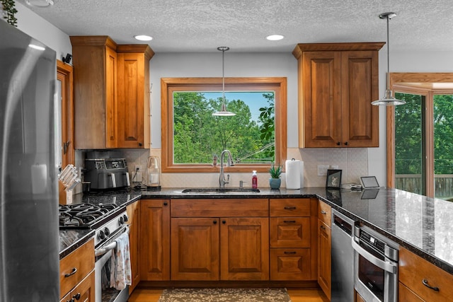 11411 Johnson Cir, Bloomington, MN 55437 - kitchen with appliances with stainless steel finishes, a sink, brown cabinetry, a textured ceiling, and dark stone countertops