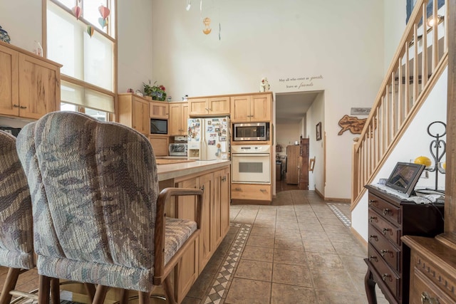 17159 Stalker Lake Rd, Battle Lake, MN 56515 - kitchen with white appliances, a towering ceiling, healthy amount of natural light, light brown cabinetry, and baseboards