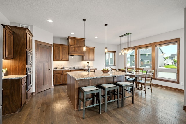 1840 Old Mill Ct, Centerville, MN 55038 - kitchen featuring a sink, dark wood-type flooring, a kitchen island with sink, a kitchen bar, and light stone counters