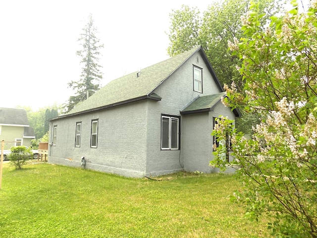 101 1st St SE, Baudette, MN 56623 - view of side of home with stucco siding, a lawn, and a shingled roof