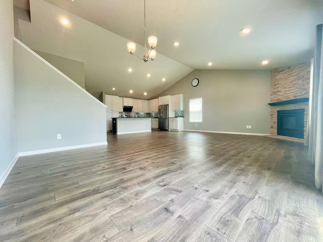 8521 Titanium Cir, Woodbury, MN 55129 - unfurnished living room featuring vaulted ceiling, a chandelier, a stone fireplace, light wood-type flooring, and baseboards