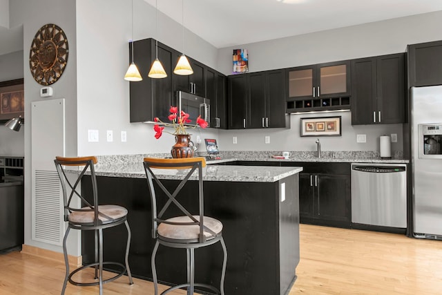 215 10th Ave S Unit 730, Minneapolis, MN 55415 - kitchen with appliances with stainless steel finishes, dark cabinets, light wood-type flooring, a kitchen breakfast bar, and a peninsula