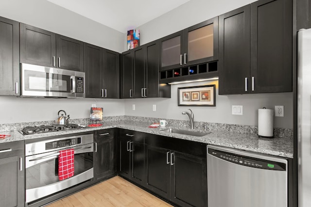 215 10th Ave S Unit 730, Minneapolis, MN 55415 - kitchen with appliances with stainless steel finishes, light wood-style floors, dark cabinetry, light stone counters, and glass insert cabinets