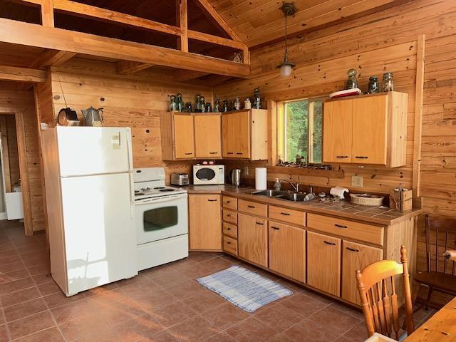 19373 Ethel Beach Rd NE, Kelliher, MN 56650 - kitchen featuring white appliances, wooden walls, a sink, tile countertops, and vaulted ceiling