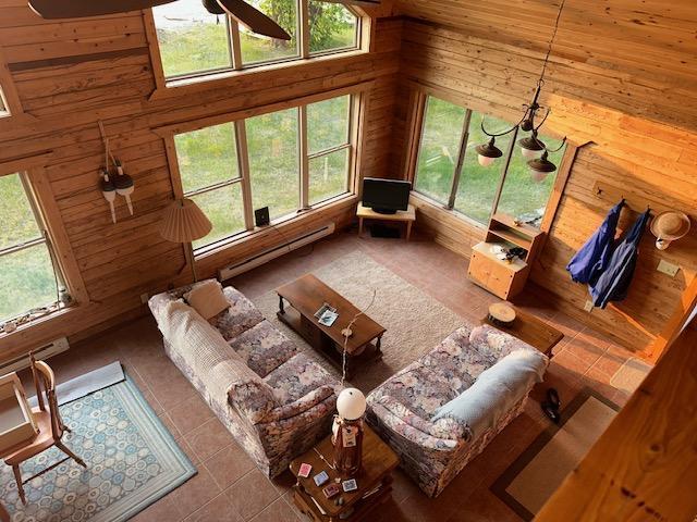 19373 Ethel Beach Rd NE, Kelliher, MN 56650 - tiled living room with wood walls, a towering ceiling, a baseboard heating unit, and a ceiling fan