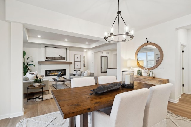 6640 Wolfberry Curv, Minnetrista, MN 55331 - dining room featuring a chandelier, light wood-style flooring, a glass covered fireplace, a tray ceiling, and recessed lighting