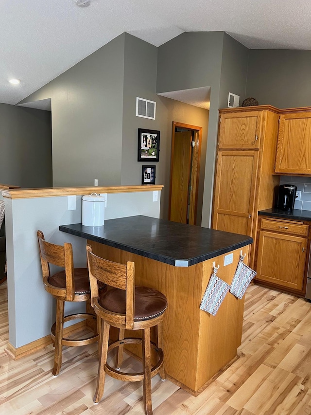 728 7th St, Litchfield, MN 55355 - kitchen featuring dark countertops, a kitchen bar, light wood finished floors, brown cabinetry, and vaulted ceiling